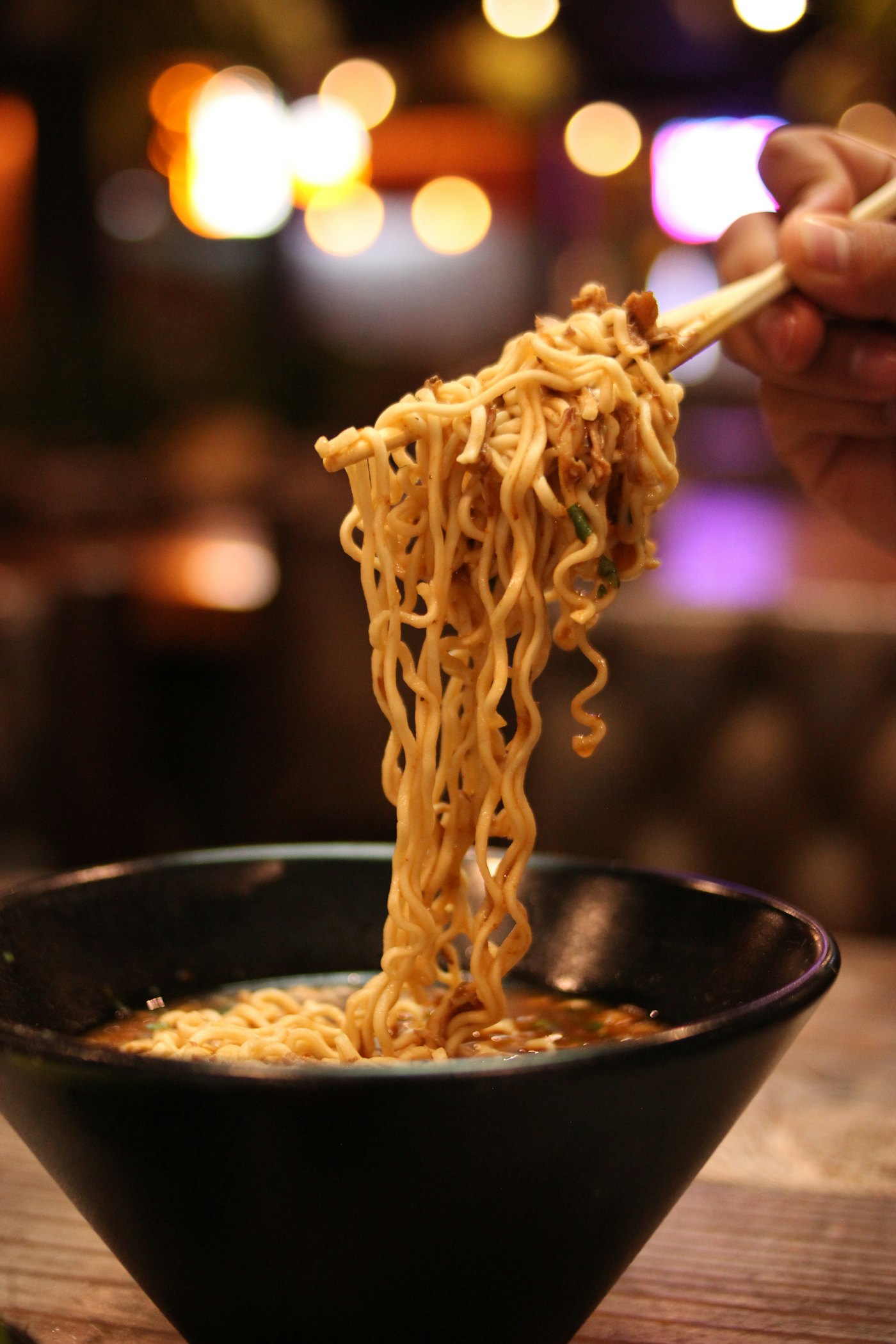Palillos levantando fideos de un bol oscuro